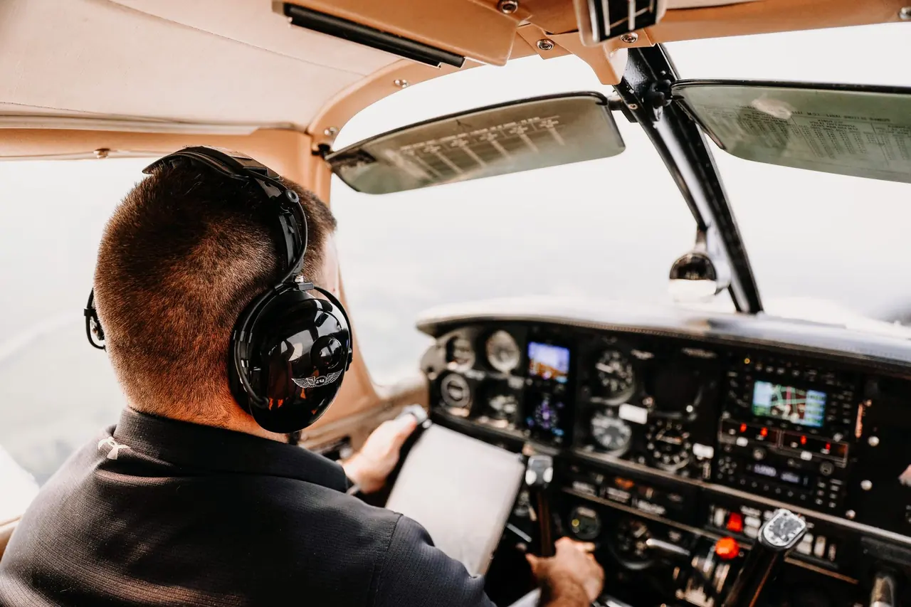 Pilot w słuchawkach prowadzący samolot, widok z tylnego siedzenia